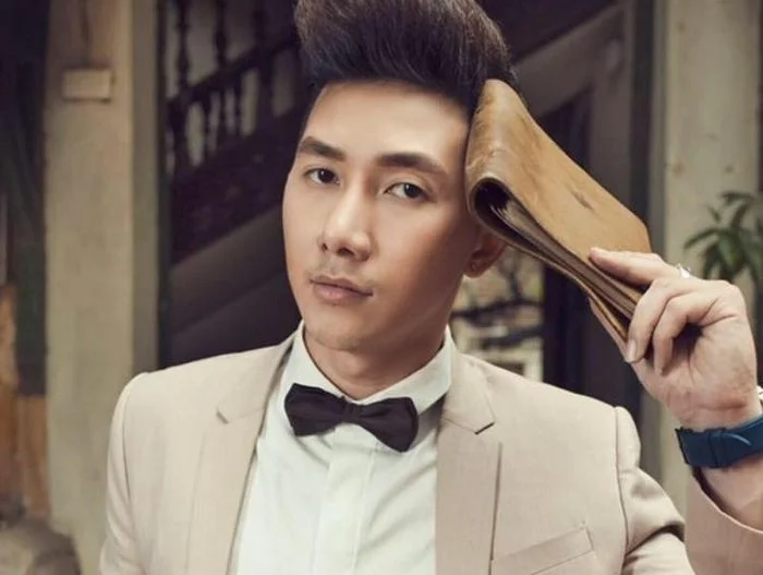 Nam người mẫu mặc vest beige, bó đinh và cầm quạt tay chụp ảnh studio.