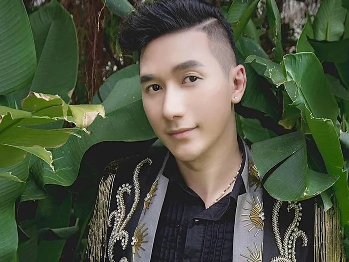 Nam người mẫu tóc đẹp, mặc áo khoác họa tiết đứng giữa lá xanh tươi.